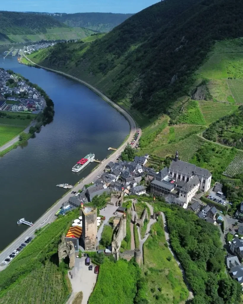 bird's eye view of a small riverside town with traditional houses, a hillside castle ruin and a ship docking at the shores of the river in Beilstein, Germany