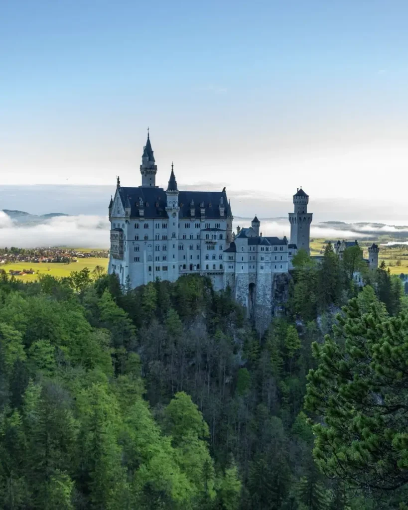 bird's eye view of the impressive Neuschwanstein Castle in Germany with lots of greenery around and lake Forggensee in the distance