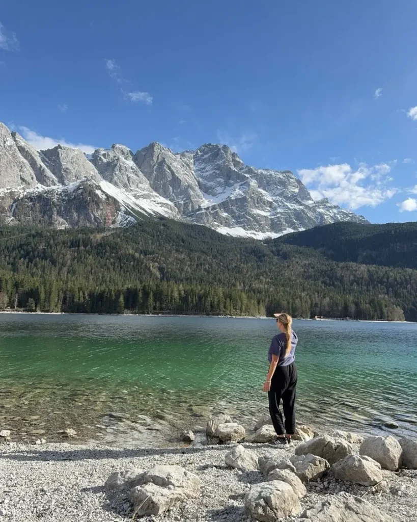 Woman standing on the rocky shores of a beautiful mountain lake with crystal-clear water with mountains in the backdrop - Eibsee