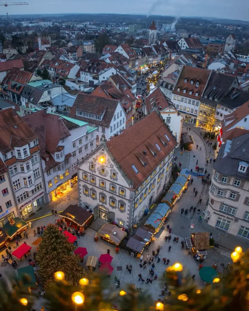 View from a tower to the old town below with christmas decorations in the foreground and beautiful house facades, christmas market stands and people below