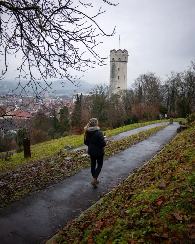 woman standing on the windy walkway up a hill and views of a white tower and old town in late autumn in Ravensburg