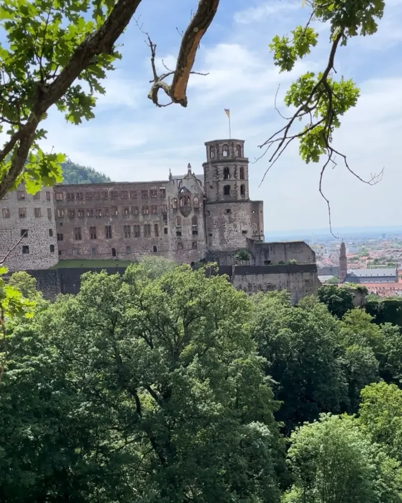 Historic castle in Heidelberg, Germany surrounded by trees and a view of the storybook city in the distance