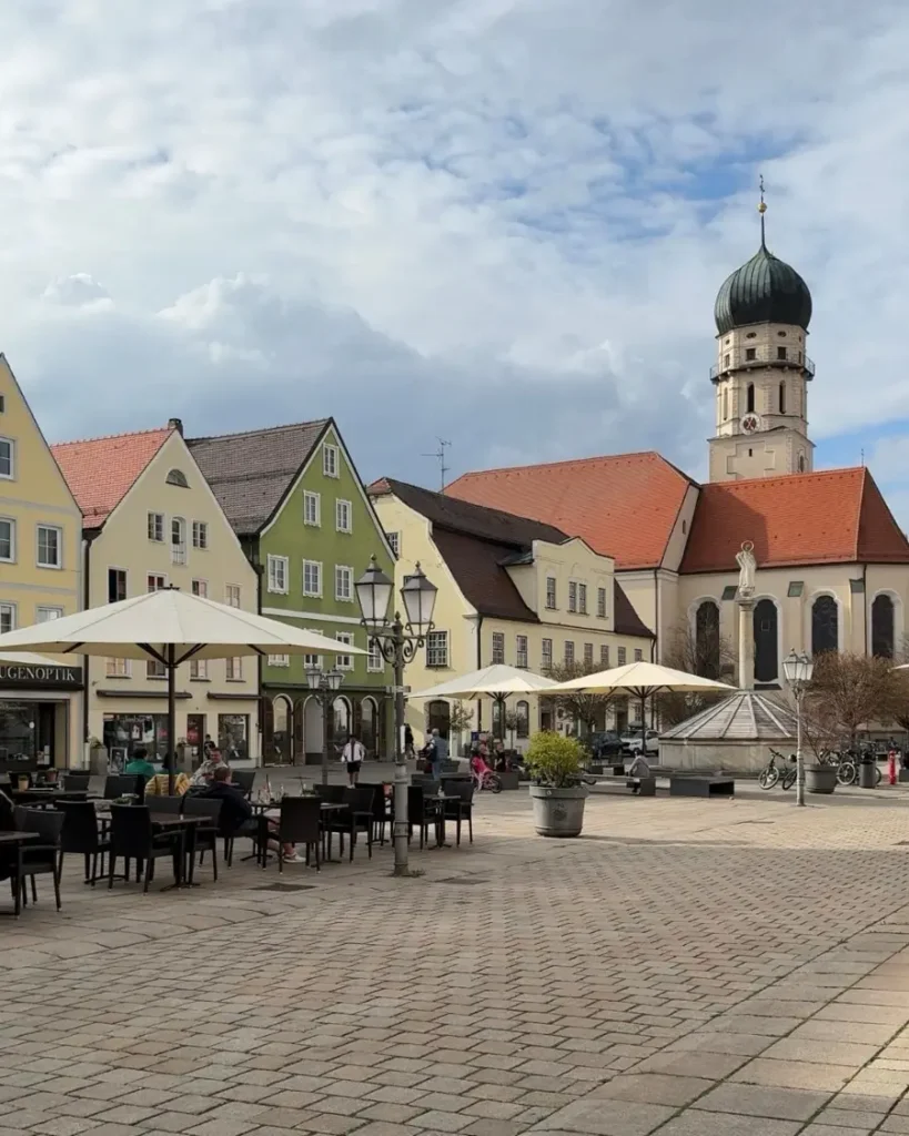 Historic center of Schongau in Germany with cobblestone roads, a church, colourful typical houses and an outdoor seating area