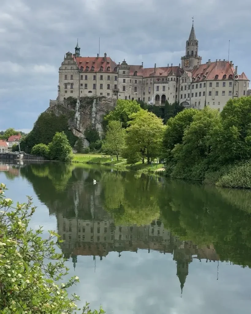 An impressive castle built on a rock along the Danube river with perfect reflections in the water and greenery around in Sigmaringen, Germany