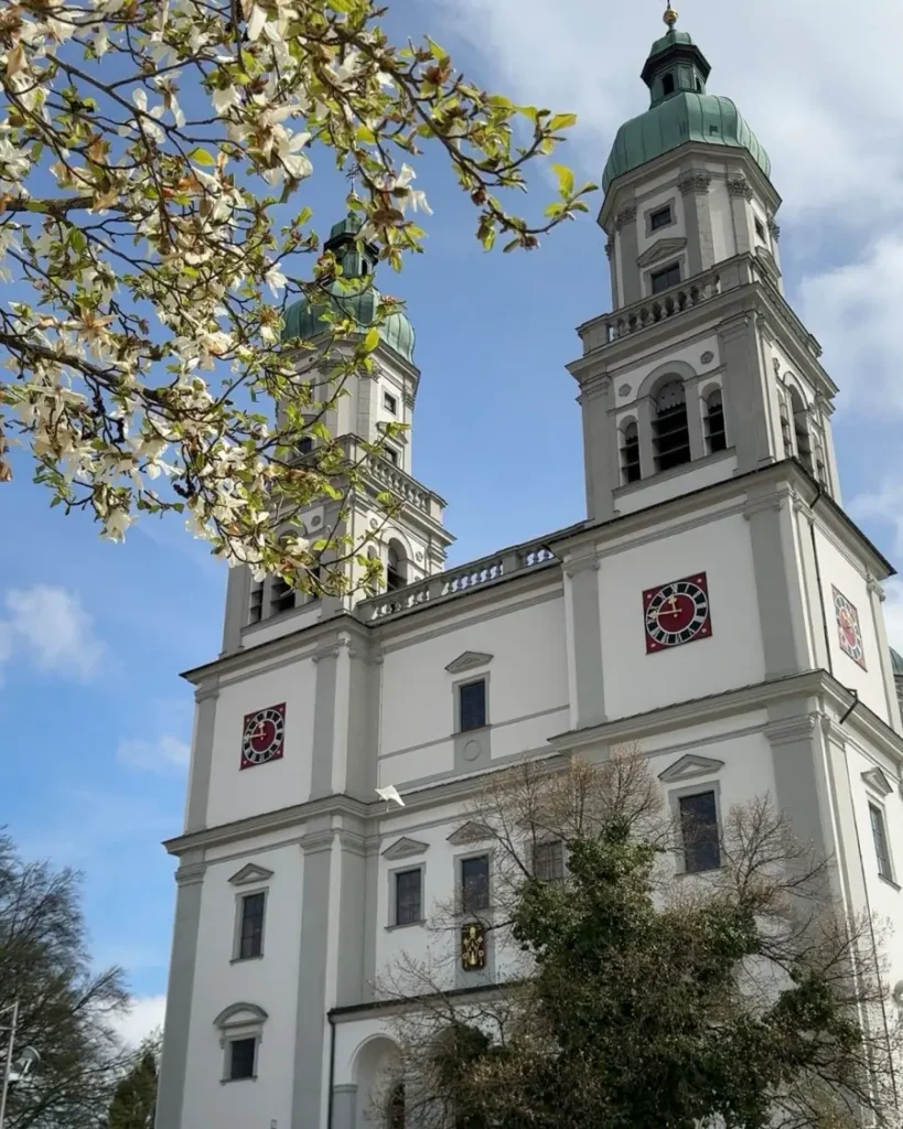 A church with two identical towers with beautiful architecture, blue skies and blooming trees in Kempten, Germany