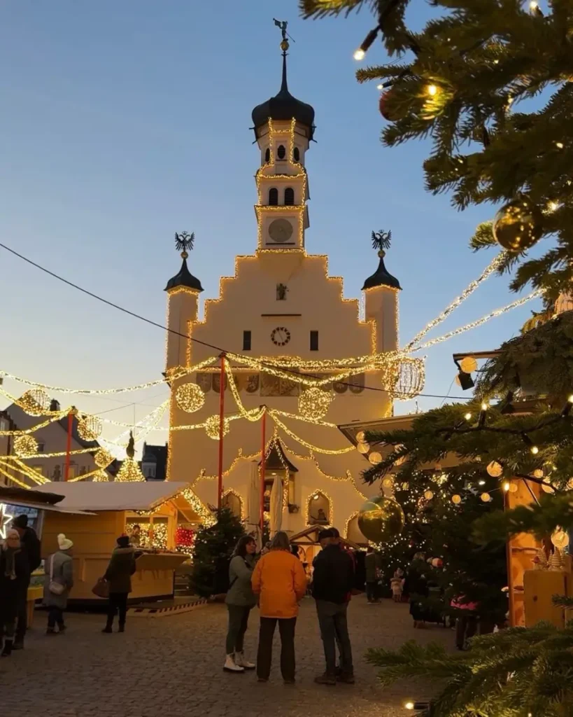 Christmas market in the historical center of Kempten with many stalls, some persons, christmas decorations and the beautiful Rathaus