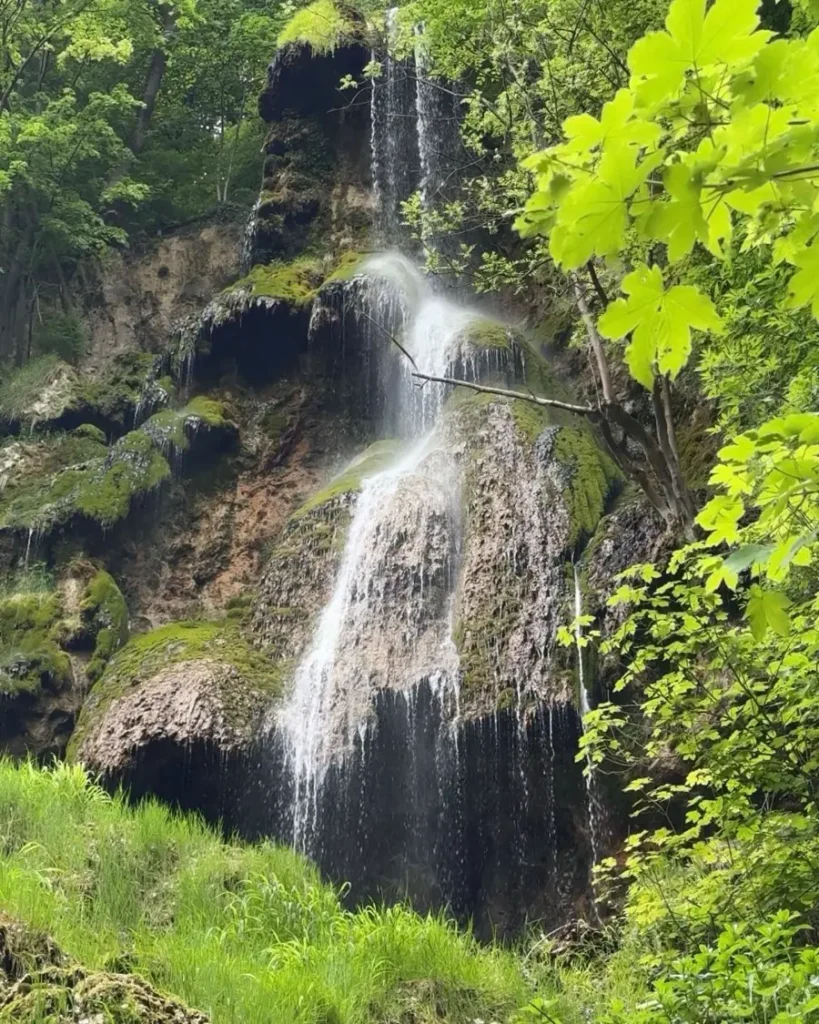 A picturesque waterfall hidden in a forest with mossy surfaces and multiple cascades with little water in Bad Urach, Germany