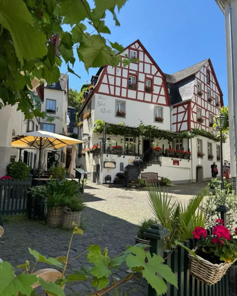 Half-timbered houses surrounded by vine and other plants on a small square with cobble stone roads and a cafe with outdoor seating area in Beilstein