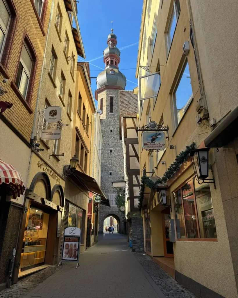 Charming alley in an old town leading to the church tower in Cochem, Germany with restaurant and shop signs