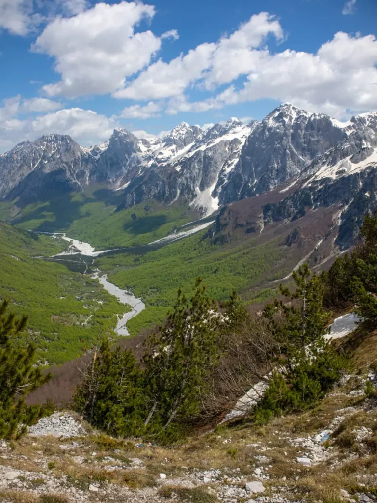 View of a lush green valley in the Albanian Alps with big, snow capped mountains in the background, Theth