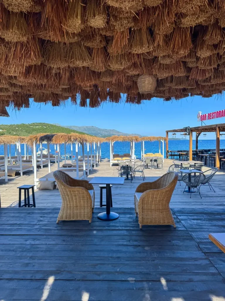 beach restaurant in Ksamil, Albania with wooden chairs, straw elements handing from the ceiling, sunbeds and ocean views