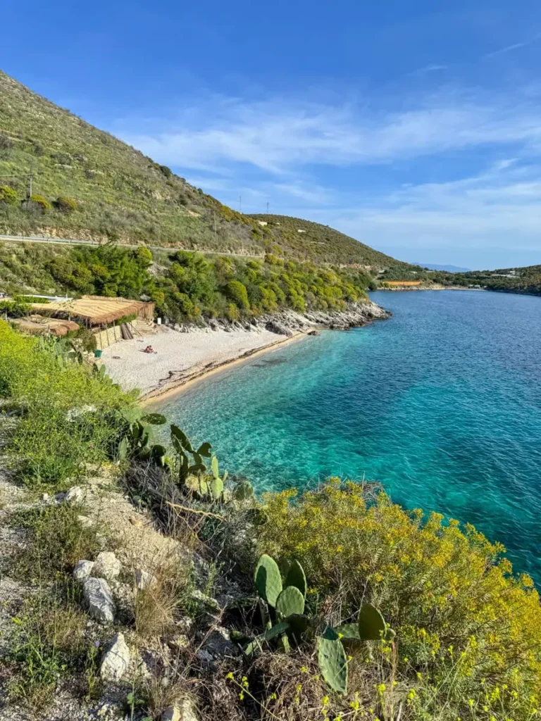 small bay along the Albanian coast with pebble stones, a wooden hut and crystal clear water surrounded by green hills in Porto Palermo