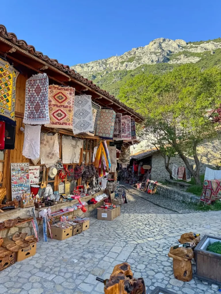 Bazar with traditional goods like colourful carpets along a cobblestone road with mountains in the distance in Kruje, Albania
