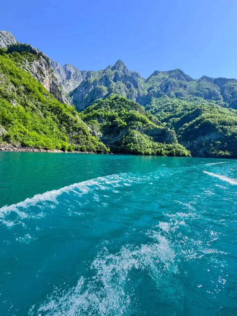 Extremely blue water of Komani lake during a boat tour with lush mountains in the backdrop - a must do activity on your Albania trip