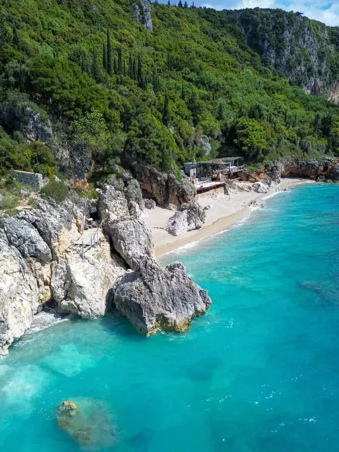 bird's eye view of turquoise water at Dhërmi beach, Albania with white pebbles, some large rocks and greenery