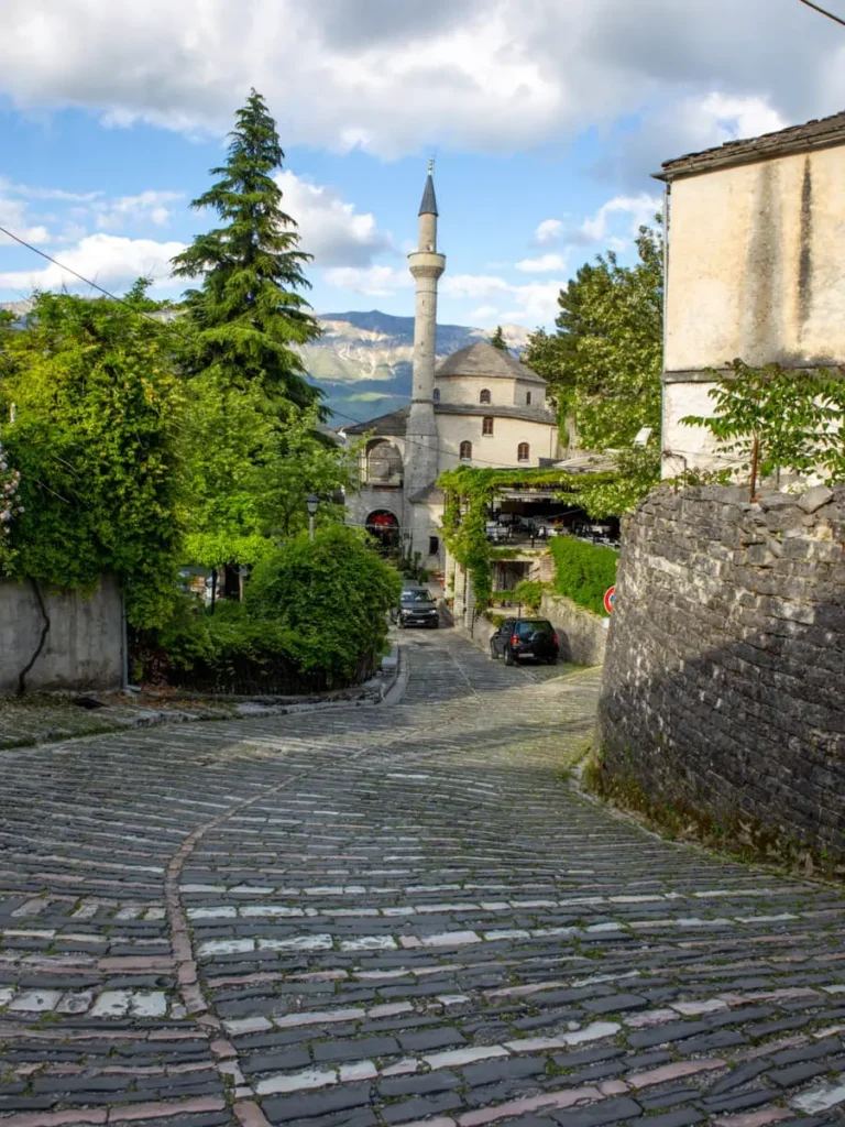 Cobblestone road leading down to a mosque in Gjirokastër, Albania with some trees and greenery around