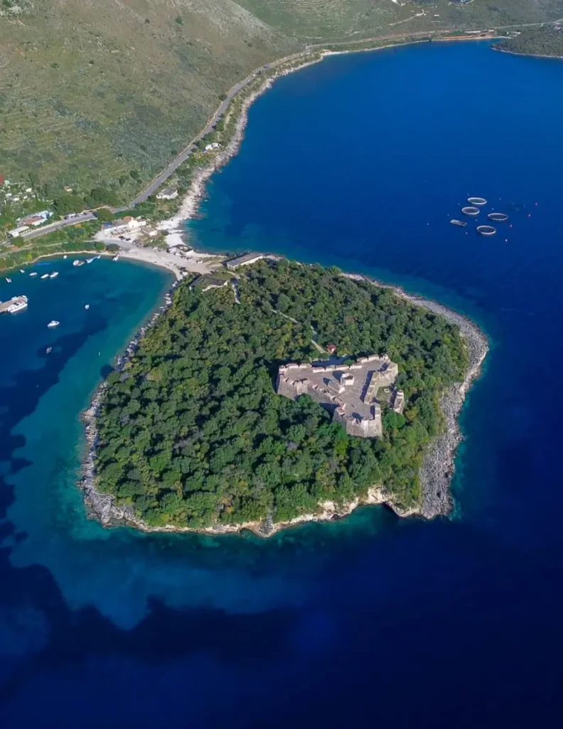 bird's eye view of a round peninsula with a castle on top, connected to the coast through a strip of sand in Porto Palermo, Albania