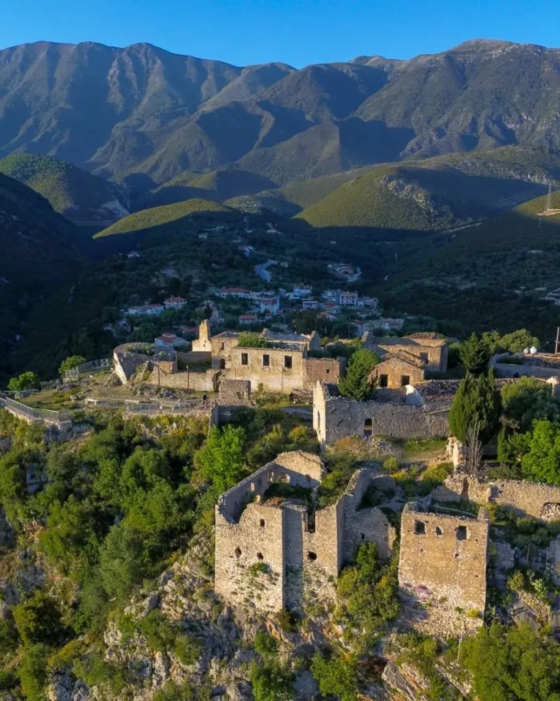 Ruins of abandoned buildings on a lush hilltop and higher mountains in the distance in Himarë, Albania