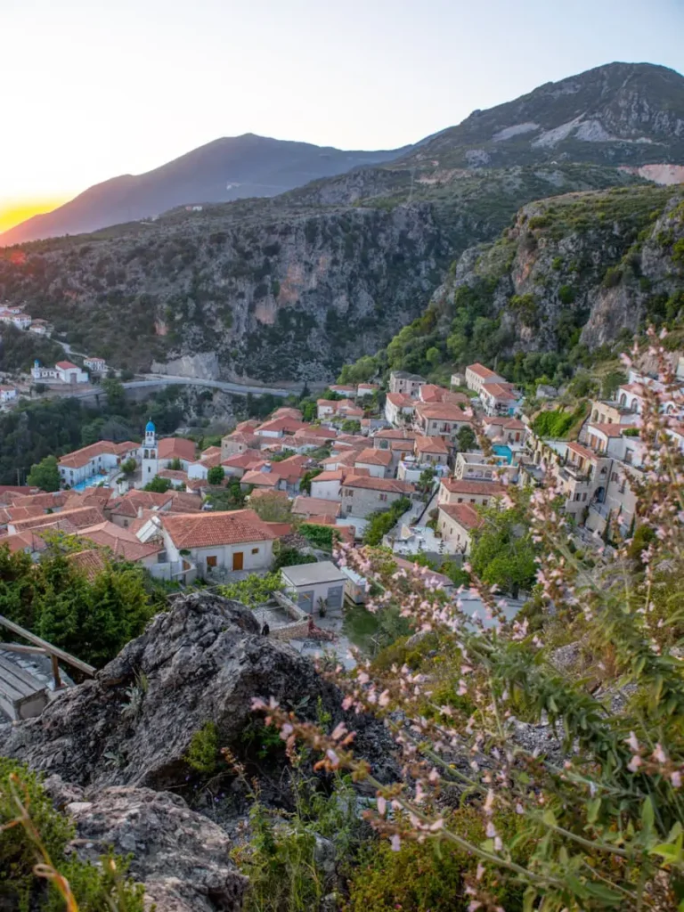 bird's eye view of Dhërmi old town in Albania with white houses and red roofs, some hills in the background and the setting sun