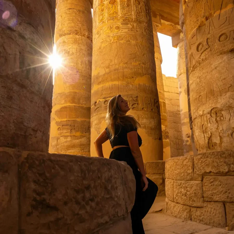 a woman dressed in black in an ancient temple, columns with detailed engraving and the sun peaking through