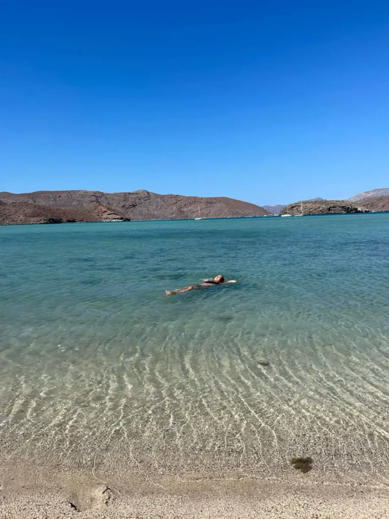 woman in a black bikini floating in a crystal clear water at a lagoon in a dry hilly landscape at playa encontrada in  baja california sur Mexico