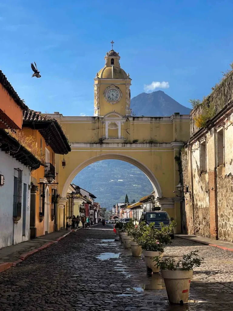 colourful town with cobblestone roads, a volcano in the backdrop and an arch with a church tower