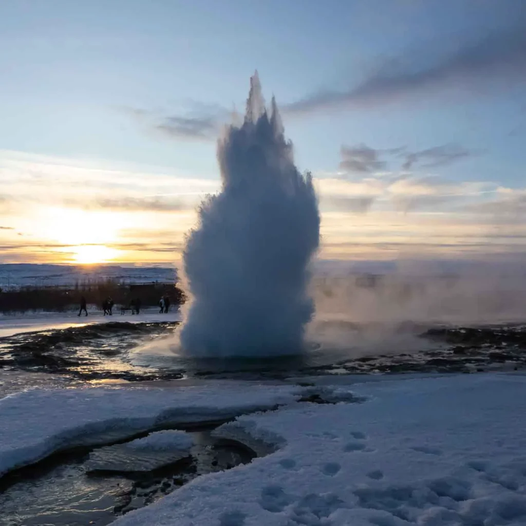 a geyser blowing water in a snowy landscape during sunset