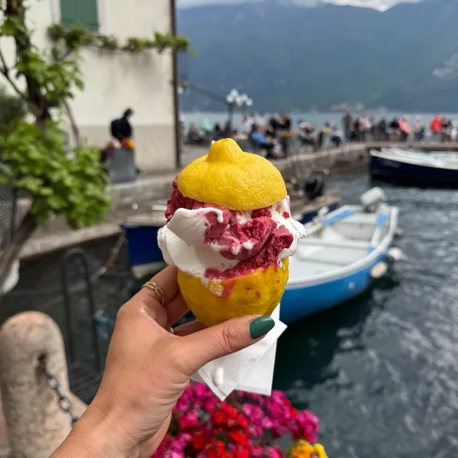 hand-held ice cream inside a real lemon with a background of a lake with some people, boat and houses