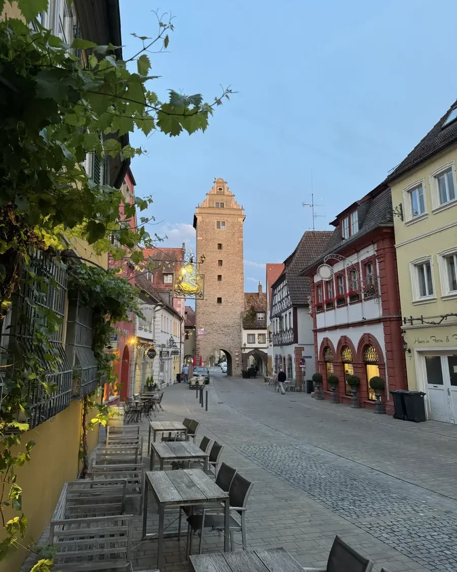Cobblestone road leaving to a historic town gate tower lined with houses, vine and outdoor seating area in Volkach am Main