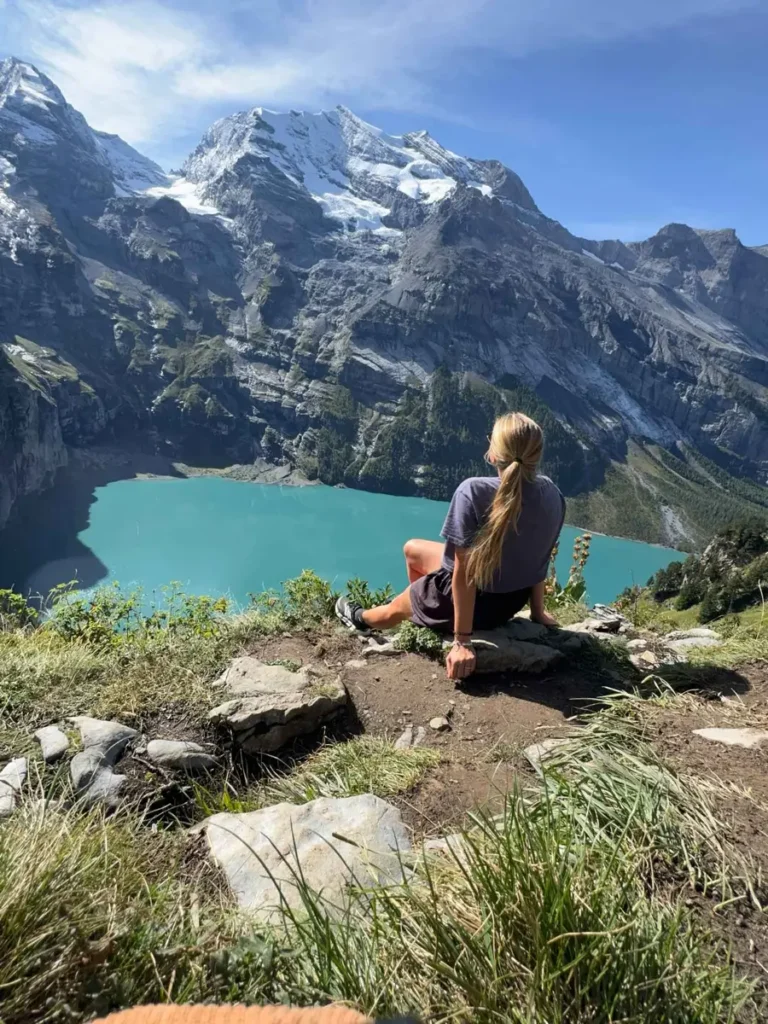 female hiker sitting o a rock overlooking a gorgeous blue lake with mountains in the backdrop