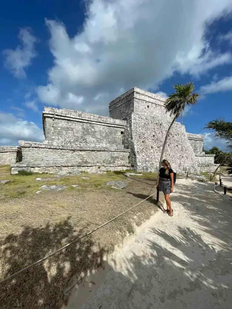 Tulum Archeological Site  old rectangular shaped buildings out of white rock and a woman looking at the site surrounded by mexican landscape in Tulum Mexico
