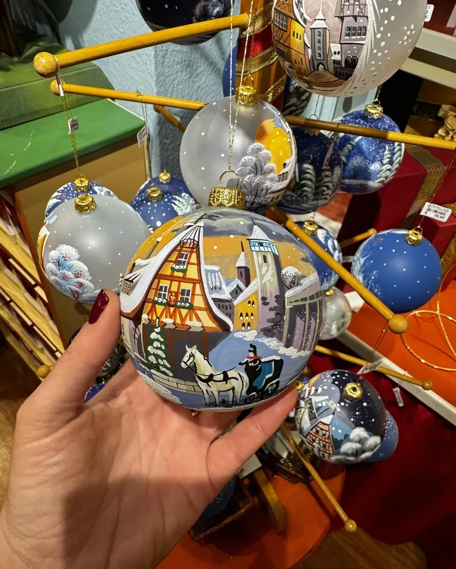 Hand holding a painted Christmas tree ornament with a half-timbered house in a gift shop in Rothenburg ob der Tauber