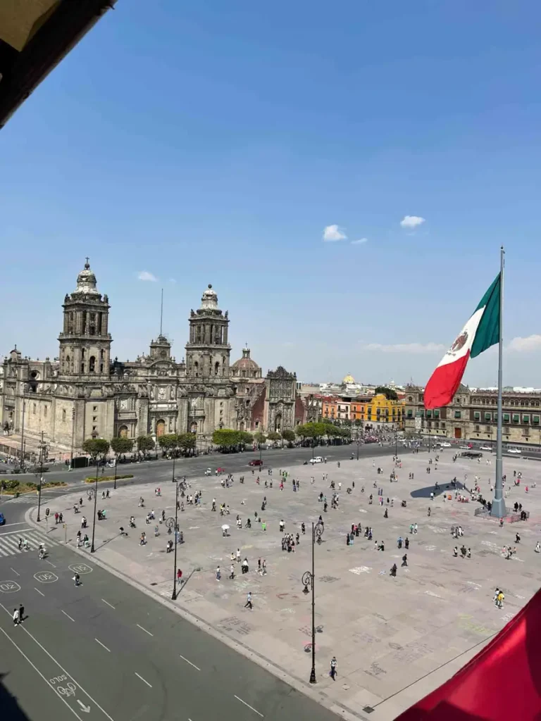 big square with a street next to it with many lanes and a old building with two towers and the mexican flag waving, zocalo Mexico City, Plaza de la Constiution - not to be missed on your Mexico itinerary