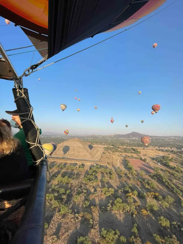 picture from a hot air ballon with multiple more in the blue sky looking down on a dry landscape close to mexico city