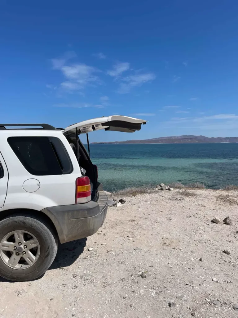 white car with an open door parked on a beach with the sea and the blue sky in the back