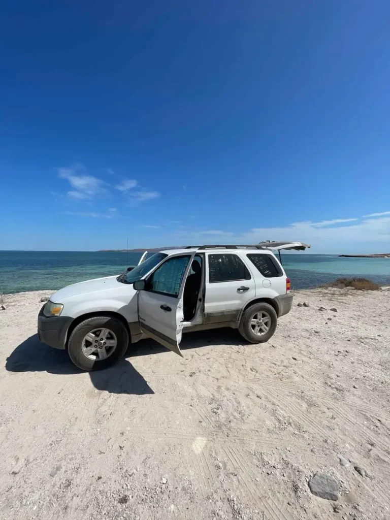 white car with an open door parked on a beach with the sea and the blue sky in the back