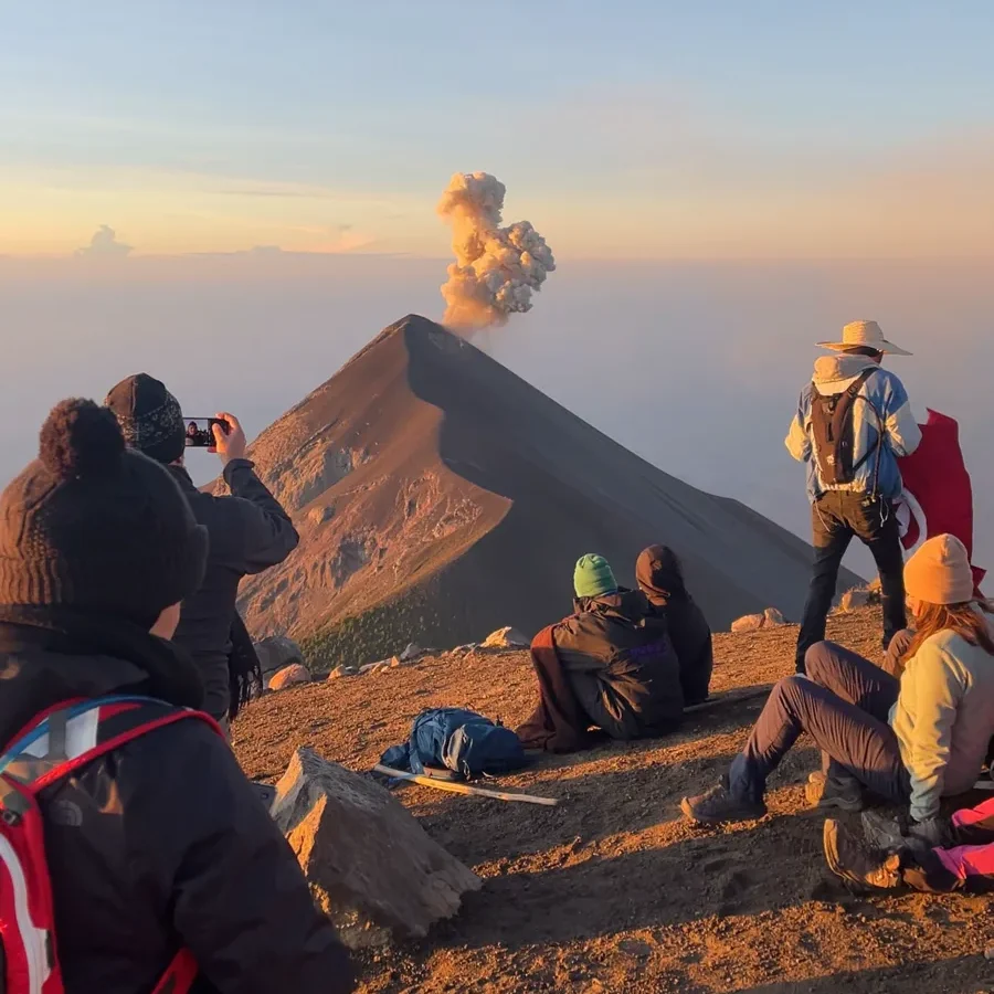 view of an erupting volcano with many hikers taking pictures during sunrise