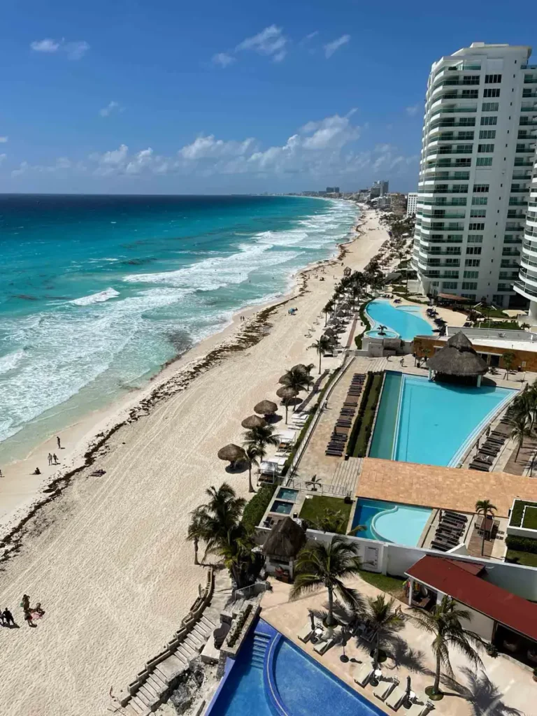 Cancun hotel zone views on the white beach with blue water and white foam from big white waves overlooking hotels pools and palm trees in Cancun