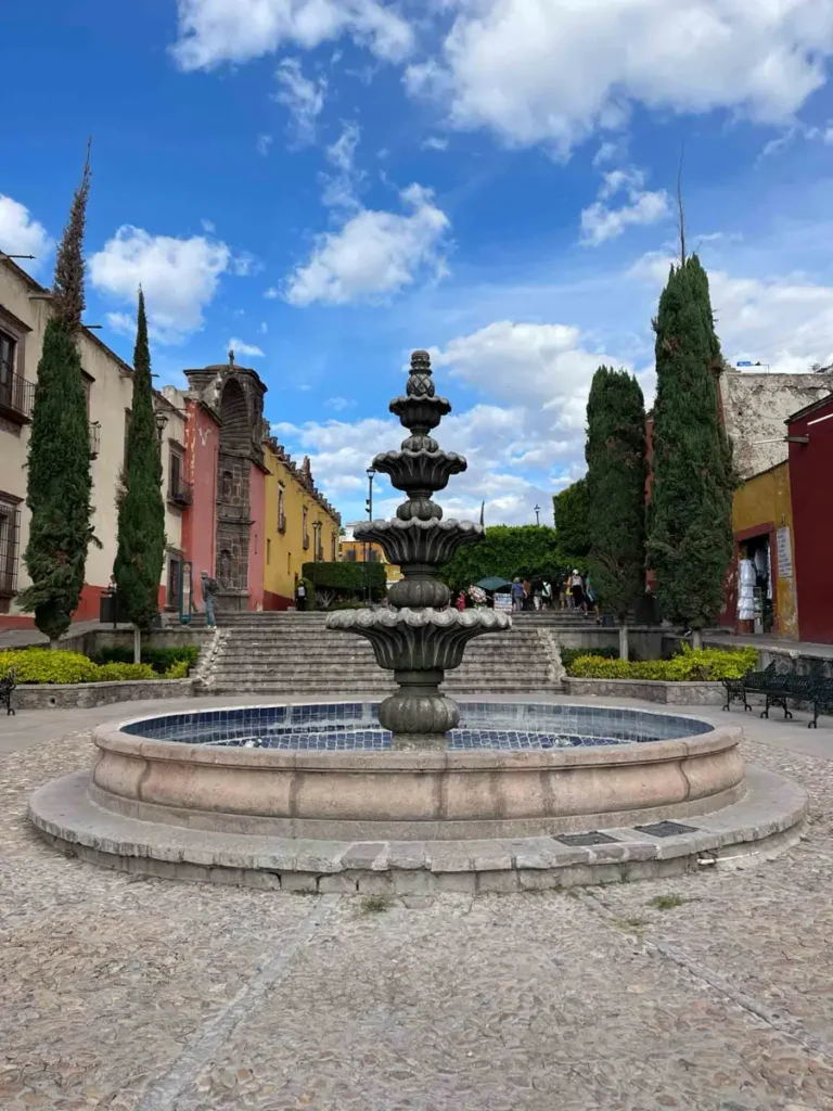 foutain surrounded by colorul houses and tall thin trees in san miguel de allende mexico