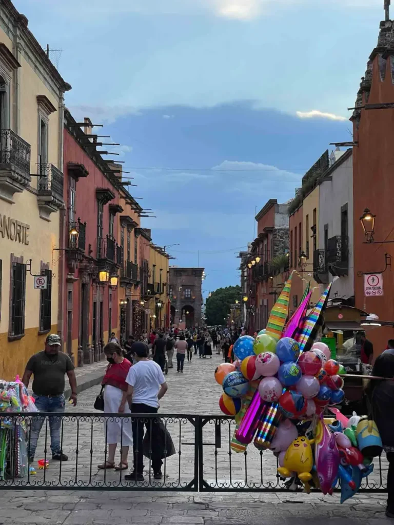 San Miguel de Allende downtown with a metal fence, colorful houses next to each other on a small pedestrian street with a lot of balloons hanging on the fence, ideal stop for your perfect Mexico itinerary