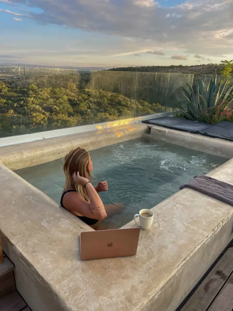 jacuzzi with a view over San Miguel de Allende at Cuna del Cielo blonde woman in a black bikini sitting in jacuzzi with a view over San Miguel de Allende and mexican nature at Cuna del Cielo with her laptop and cup