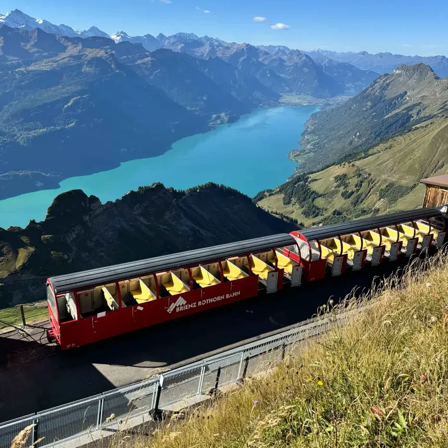 train standing on top of a mountain with views of a very blue lake and green hills