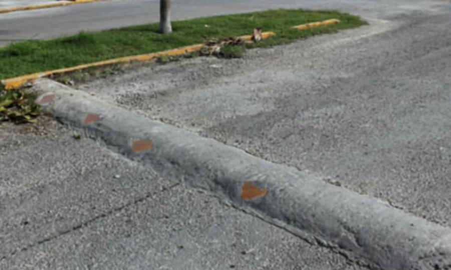 speed bump on an asphalt street next to a small traffic island with grass and a traffic sign 