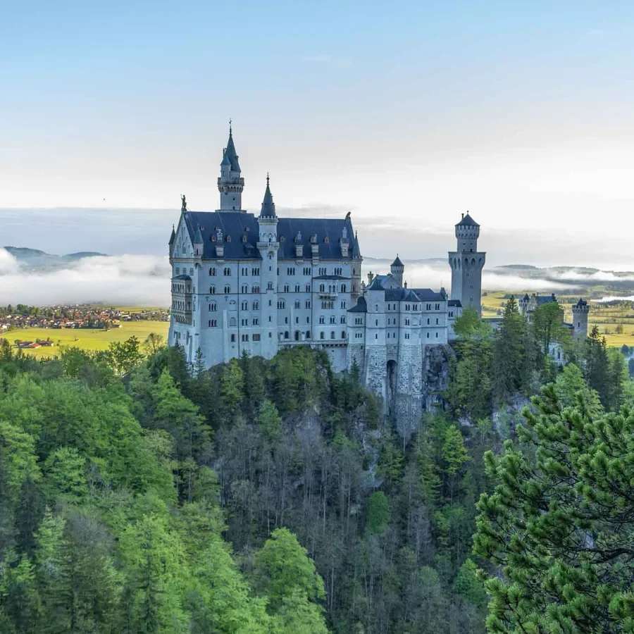 bird's eye view of a large white castle with multiple towers surrounded by forest with a lake in the distance