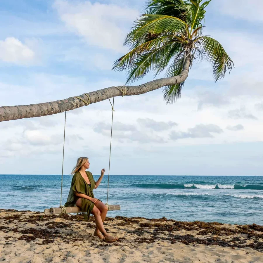 a woman sitting on a swim that's set up on a palmtree on a beach with some algae and white sand