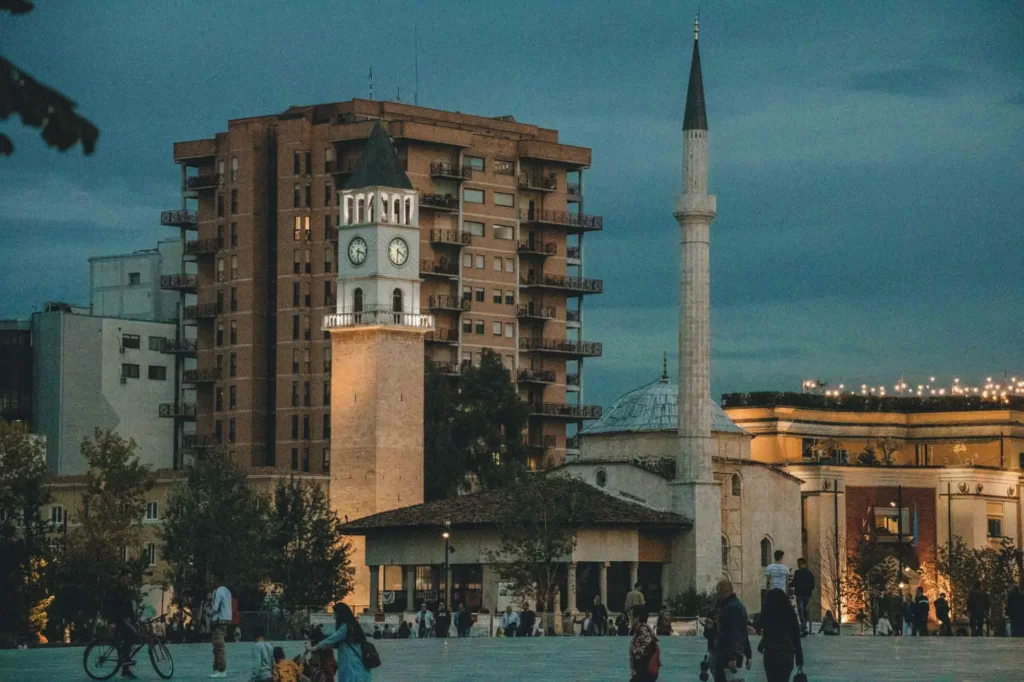 city square in Tirana, the capital of Albania with a large building, some poeple. a mosque and lights