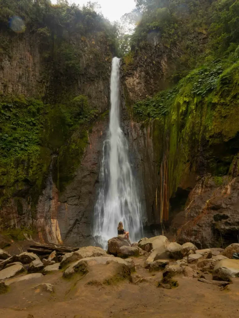 long thin waterfall forming a round body of water surrounded by rocks, overgrowns green rocks and the jungle in bajos del toro in costa rica