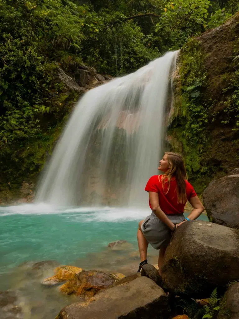 Blue Falls Catarata La Celestial waterfall forming a blue body of water surrounded by rocks, overgrown rocks and the jungle in bajos del toro costa rica