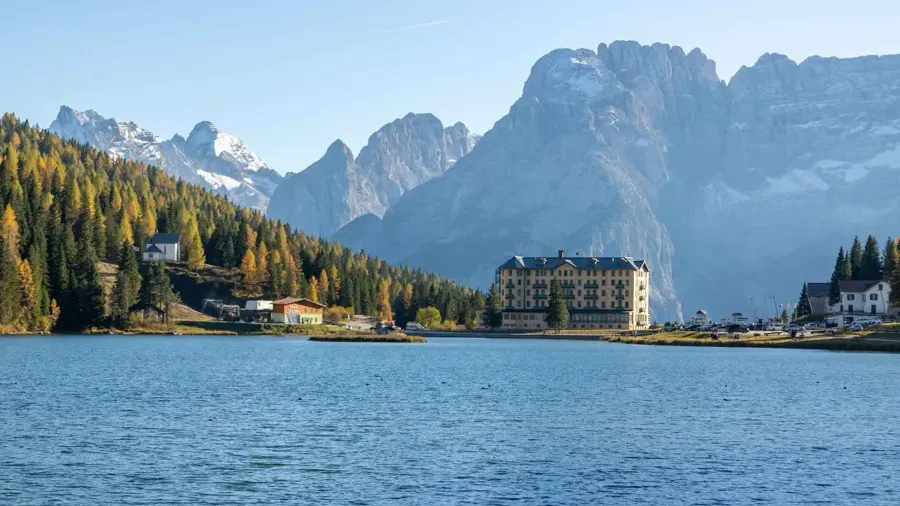 A scenic mountain lake with majestic mountain peaks in the backdrop and a single house in the distance at Lago di Misurina in the Dolomites