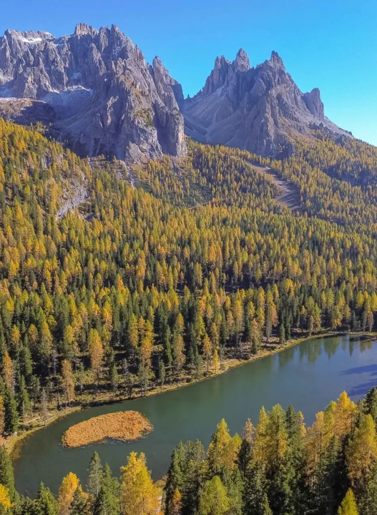 bird's eye view of a stunning mountain lake with a heart-shaped island surrounded by golden larches and towering mountain peaks - Lago di Antorno in the Dolomites